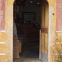 Fotoaufnahme des Eingangs zum Gelände. Im Raum dahinter ist die Museumskasse  erkennbar, sie befindet sich im Korbhaus aus Knittelsbach. Über der geöffneten Holztür steht „JAL 1812“.