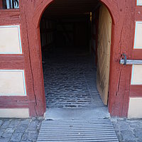 Fotoaufnahme des Haupteingangs vom Bauernhaus aus Unterlindelbach am aktuellen Standort. Vor der Schwelle der geöffneten Holztür liegt eine Rampe.  An der Hauswand rechts im Bild wurde ein Geländer aus Holz angebracht. 