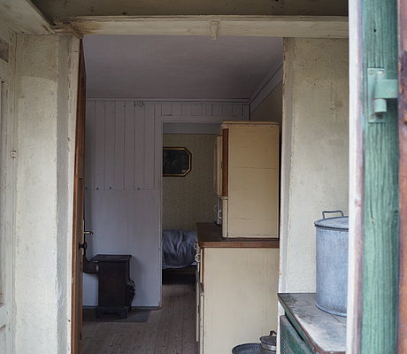 Blick in die Stube des Behelfsheimes mit Küchenschrank und Holzofen