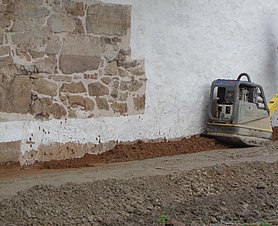 Rüttelplatte auf angeschüttetem Lehm vor Mauer