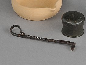 ein metallenes Objekt mit Rillen und Biegungen, daneben ein Tonschälchen mit Henkel und zwei Metallgefäse