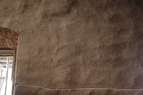 Eine Wand mit Lehmputzoberfläche mit unruhiger, unebener Gestaltung