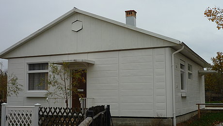 Ein in weiß gehaltenes Haus, ganz aus Stahl, mit Gartenzaun