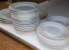 In einem Regal liegen viele weiße Teller. Die Teller sind gestapelt.