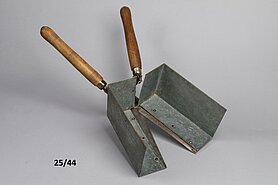Die Schere hat Holzgriffe. An den Schneiden sind Blechkästen angebracht. Der Blechkasten schließt sich, wenn die Schere geschlossen wird.