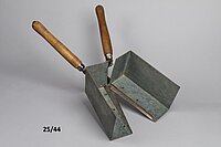 Die Schere hat Holzgriffe. An den Schneiden sind Blechkästen angebracht. Der Blechkasten schließt sich, wenn die Schere geschlossen wird.