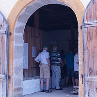 Fotoaufnahme des Eingangsbereichs vom Kommunbrauhaus aus Schlüsselfeld am aktuellen Standort. Die zweiflüglige Holztür ist nach außen geöffnet, im Inneren befindet sich eine Besuchergruppe. Der Boden vor dem Gebäude ist gepflastert. 