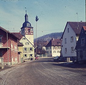 Ansicht einer Straße mit Kirchrutm und einigen anderen Häusern. Kopfsteinpflaster