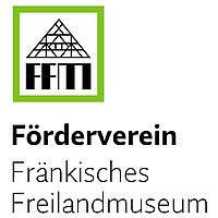 Abbildung des Logos des Fördervereins Fränkisches Freilandmuseum e.V., der Name steht in der unteren Hälfte. In einem rechteckigen Rahmen darüber stellen die Abkürzung „FFM“ und ein gezeichneter Fachwerkgiebel ein Haus dar.