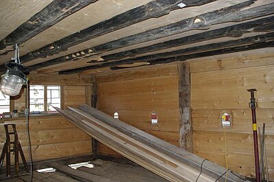 Das Bild zeigt eine Stube. Wände und Decke sind aus Holz. Die Decke ist verziert. Die Verzierungen sind geschnitzt.