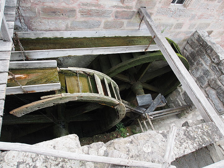 0)	Das Foto zeigt das kaputte Mühlrad in der Radstatt am Mühlengebäude. Der Radkranz ist gebrochen.