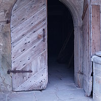 Fotoaufnahme des Eingangs zum Hofbrauhaus aus Kraisdorf. Die rechte Hälfte der zweiflügligen Holztür ist nach außen geöffnet. Der Boden außen und innen ist mit unregelmäßigen Steinplatten gepflastert. 