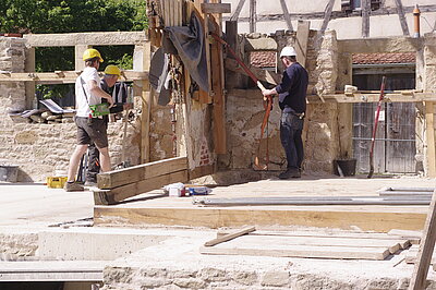 Bauarbeiter positionieren eine eingeschalte Fachwerkwand, die an einem Kran hängt
