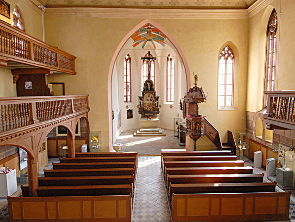 Fotoaufnahme des Innenraums der Spitalkirche mit den beiden Emporen. Der Altar befindet sich mittig im Kirchenschiff, rechts steht die erhöhte Kanzel. Davor sind einige Reihen mit Bänken. 