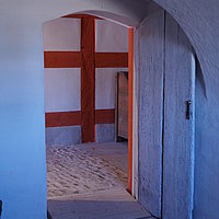 Fotoaufnahme des Eingangs zur Küche im Bauernhaus Unterlindelbach am aktuellen Standort. Vor der Schwelle der Holztür liegt eine Rampe. Der Boden ist gepflastert. 