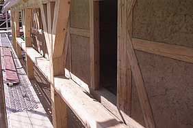 Außenansicht eines Holzfachwerks mit Lehmfüllungen und  einer Türöffnung.