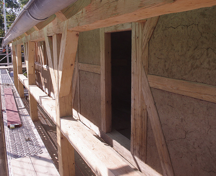 Außenansicht eines Holzfachwerks mit Lehmfüllungen und  einer Türöffnung.