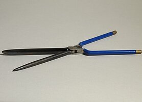Das Onduliereisen sieht aus wie eine Schere. Es hat blaue Griffe mit goldfarbenen Enden. Das eine Eisen ist ein runder Stab. Das andere Eisen ist eine hohle Form. In sie passt der runde Stab hinein.