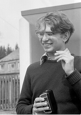 Auf dem Bild ist ein junger Mann. Es ist Konrad Bedal. Er lacht und hält eine Kamera.