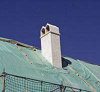 eine Kamin mit einer doppelzügigen Schlothaube, weiß, in Mitten einer noch mit Folie gedeckten Dachansicht