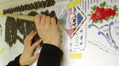 Zwei Hände stupfen mit einem Pinsel durch eine Schablone bunte Muster an eine Wand