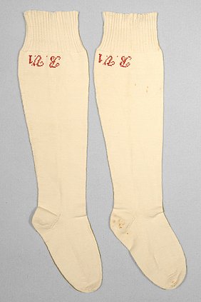 Die beiden Socken sind weiß. Sie sind mit roten Buchstaben bestickt. Die Buchstaben sind Abkürzungen für einen Namen.