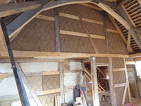 Bogenförmige Holzkonstruktion vor hoher Fachwerkwand. Innenansicht des Betsaals