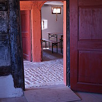 Fotoaufnahme der Tür zur Stube im Bauernhaus aus Unterlindelbach am aktuellen Standort. Vor der Schwelle der Holztür liegt eine Rampe. Im Raum dahinter steht eine Bierzeltgarnitur. 