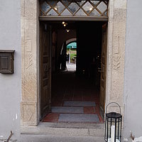 Fotoaufnahme des Haupteingangs vom Gasthaus zur Krone am aktuellen Standort. Zur nach innen geöffneten Holztür führt eine Steinstufe, darauf steht rechts eine Laterne mit Kerze. Davor liegt ein Fußabstreifer. Über der Tür hängt eine Lampe, links daneben ein Briefkasten. 