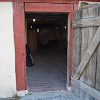 Fotoaufnahme des Eingangs zum Kuhstall aus Unterlindelbach am aktuellen Standort. Die Holztür ist nach außen geöffnet. Der Boden im Inneren ist gepflastert, das Dach mit Sechseck-Flachziegeln gedeckt. 