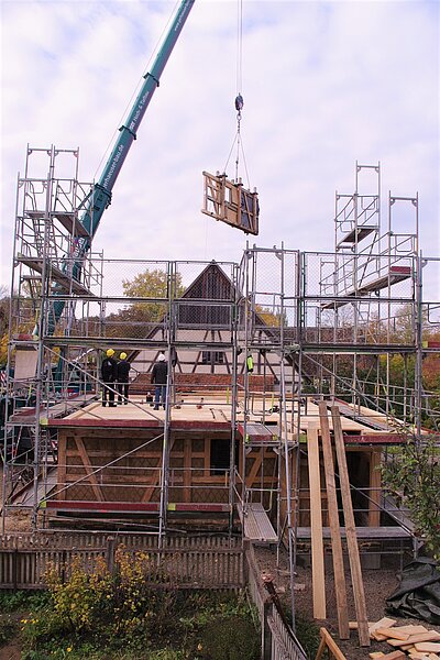 Hausbaustelle mit Autorkran und daran schwebendem Wandteil