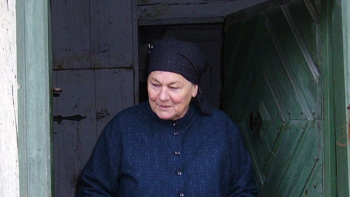 Fotoaufnahme der Führung „Zu Besuch bei Maria Dörfler“. In der geöffneten Tür des Bauernhauses aus Oberzettlitz steht eine als Maria Dörfler kostümierte Museumsführerin. Sie trägt einen zugeknöpften Kittel und ein Kopftuch. 