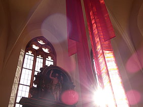 Textile rote Bahnen vor den gotischen Fenstern und dem Altar im Chorraum der Spitalkirche
