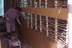 ein Bauhofmitarbeiter beim Lehmbewurf eines mit Haselnussruten abgeflochtenen Wandteil
