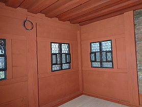 rot gestrichene Bohlenstubenwände mit Butzenscheibenfenster