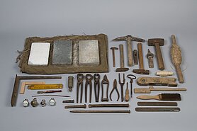 Auf dem Bild sind Werkzeuge. Es sind Hämmer, Zangen, Meißel, Schleifsteine, eine Wasserwaage, eine Schnur, ein Zollstock und Winkel.