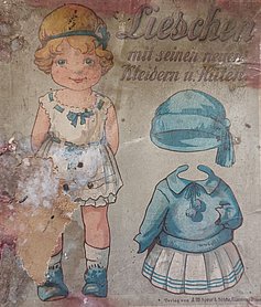 Auf dem DEckel ist ein Kind abgebildet. Es trägt Unterwäsche. Daneben sind eine Mütze und ein Kleid. Beides ist blau.