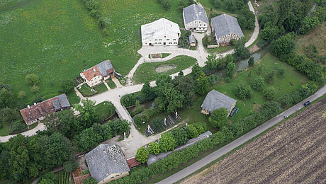 Fotoaufnahme eines Luftbildes der Baugruppe Süd. Das Bild wurde von Süden aus aufgenommen. Die einzelnen Gebäude sind durch Wege miteinander verbunden. Umliegend befinden sich Felder, Wiesen und Bäume.