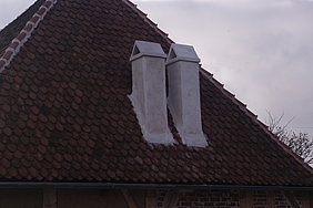 Zwei weiße Schornsteine auf einem Walmdach, das mit Ziegeln gedeckt ist.