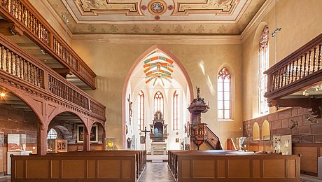 Fotoaufnahme des Innenraums der Spitalkirche von hinten. Im Vordergrund befinden sich mehrere Reihen mit Sitzbänken. An den Seiten ziehen sich Emporen mit verzierten Holzgeländer entlang. Im Hintergrund sind die hölzerne Kanzel und der Altar erkennbar. 