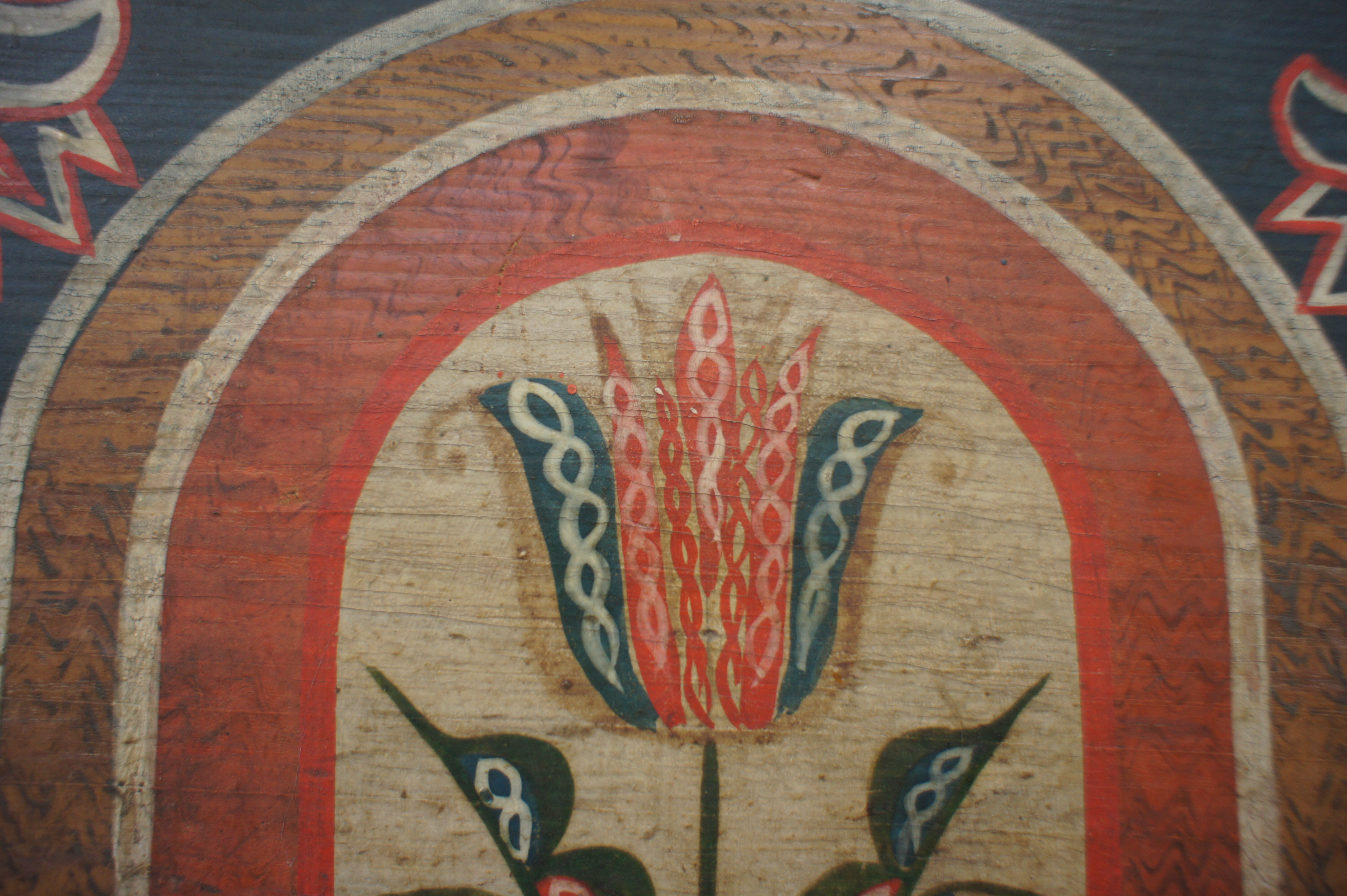 Fotoaufnahme einer gemalten Tulpe, welche sich auf einen Holzmöbel, vermutlich einen Schrank, befindet. Um die Tulpe herum wurden mehrere Rundbögen gemalt. 