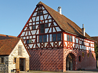 Fotoaufnahme des Amtshauses aus Obernbreit am aktuellen Standort. Das Fachwerkhaus wird von der Sonne beschienen. 